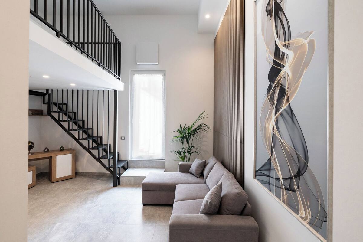 Een moderne woonkamer met een trap, een groot abstract schilderij en een potplant.