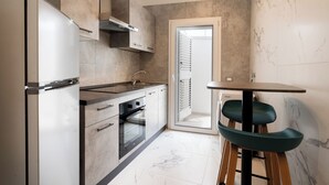 A compact kitchen with a built-in oven, a refrigerator, and a small dining area with a table and stools.