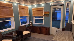 A cozy room with wicker furniture, a small table, and a view of the outdoors through large windows with blinds. - Escape to this charming beach cottage along the coast of Broadkill Beach (Milton)