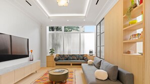 Un salón moderno con un sofá gris, un tapete colorido, una estantería de madera y un televisor grande en la pared.