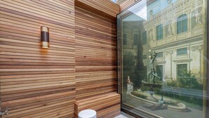 Une façade moderne avec des panneaux de bois horizontaux, une fenêtre en verre qui reflète un bâtiment classique et un petit tabouret blanc.