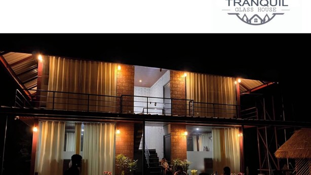 A two-story building with a glass facade, outdoor seating area, and a thatched roof structure. - Tranquil Glass House  By Coorg Tree House (madikeri)