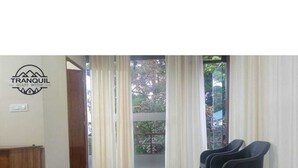 A room with a bed, two chairs, and a view of a balcony with trees. - Tranquil Glass House  By Coorg Tree House (madikeri)