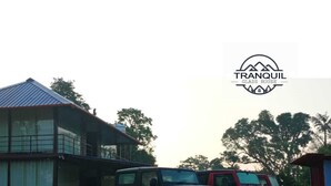 A modern house with a glass extension, two SUVs parked in front, and a logo for 'TRANQUIL GLASS HOUSE'. - Tranquil Glass House  By Coorg Tree House (madikeri)