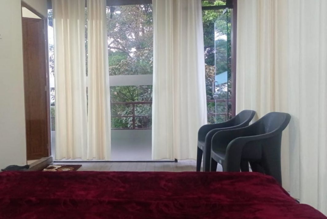 Una habitación con cama, dos sillas y vistas a un balcón con árboles.