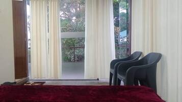 Una habitación con cama, dos sillas y vistas a un balcón con árboles.