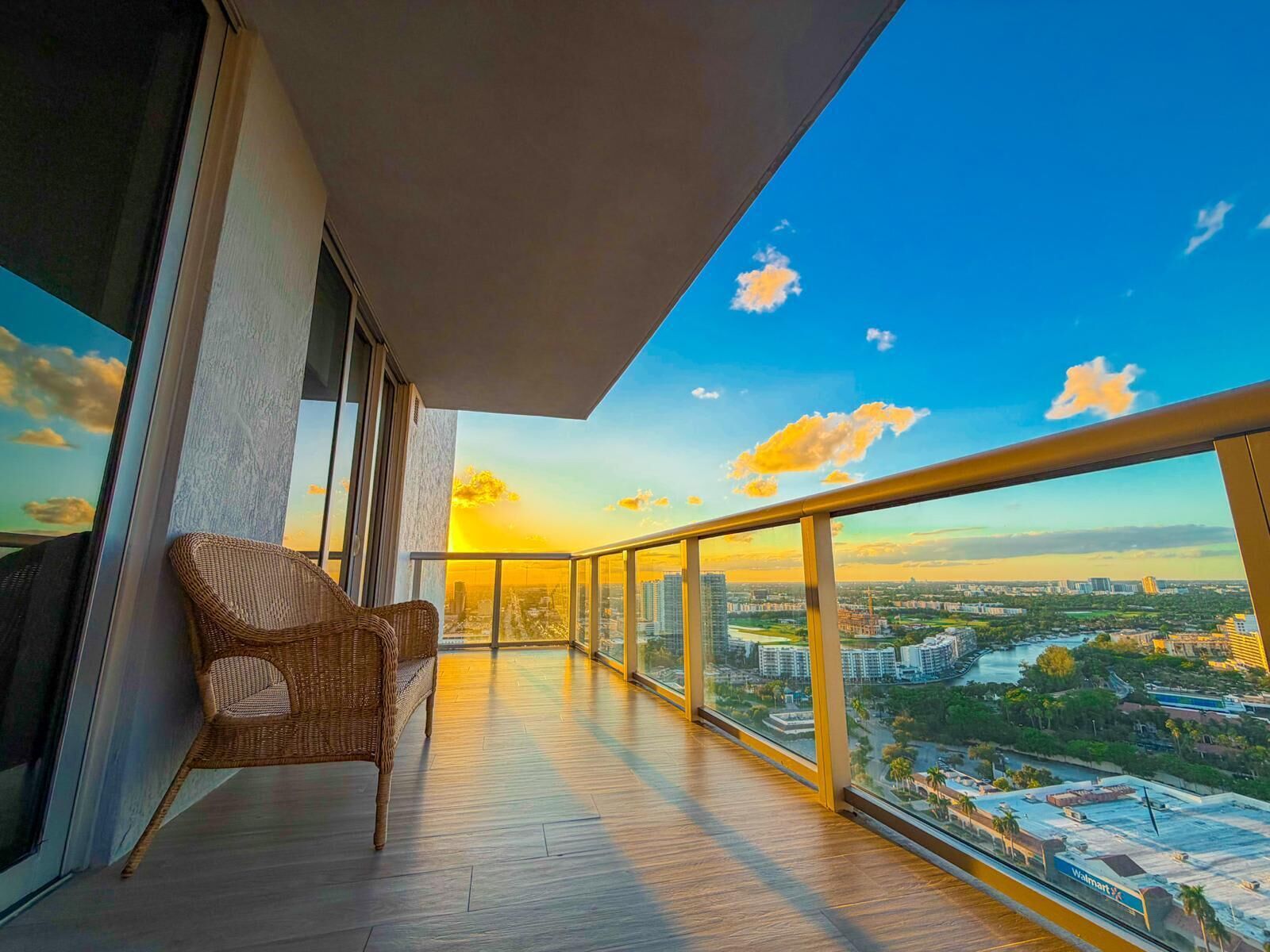 A balcony with a wicker chair, a view of a cityscape, and a clear sky.