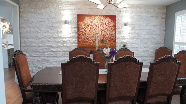 A dining area with a stone wall, a large painting, and six chairs with ornate backs.