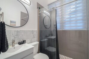 Un baño moderno con un lavabo blanco, un inodoro, un espejo grande y una ducha con cerramiento de vidrio.