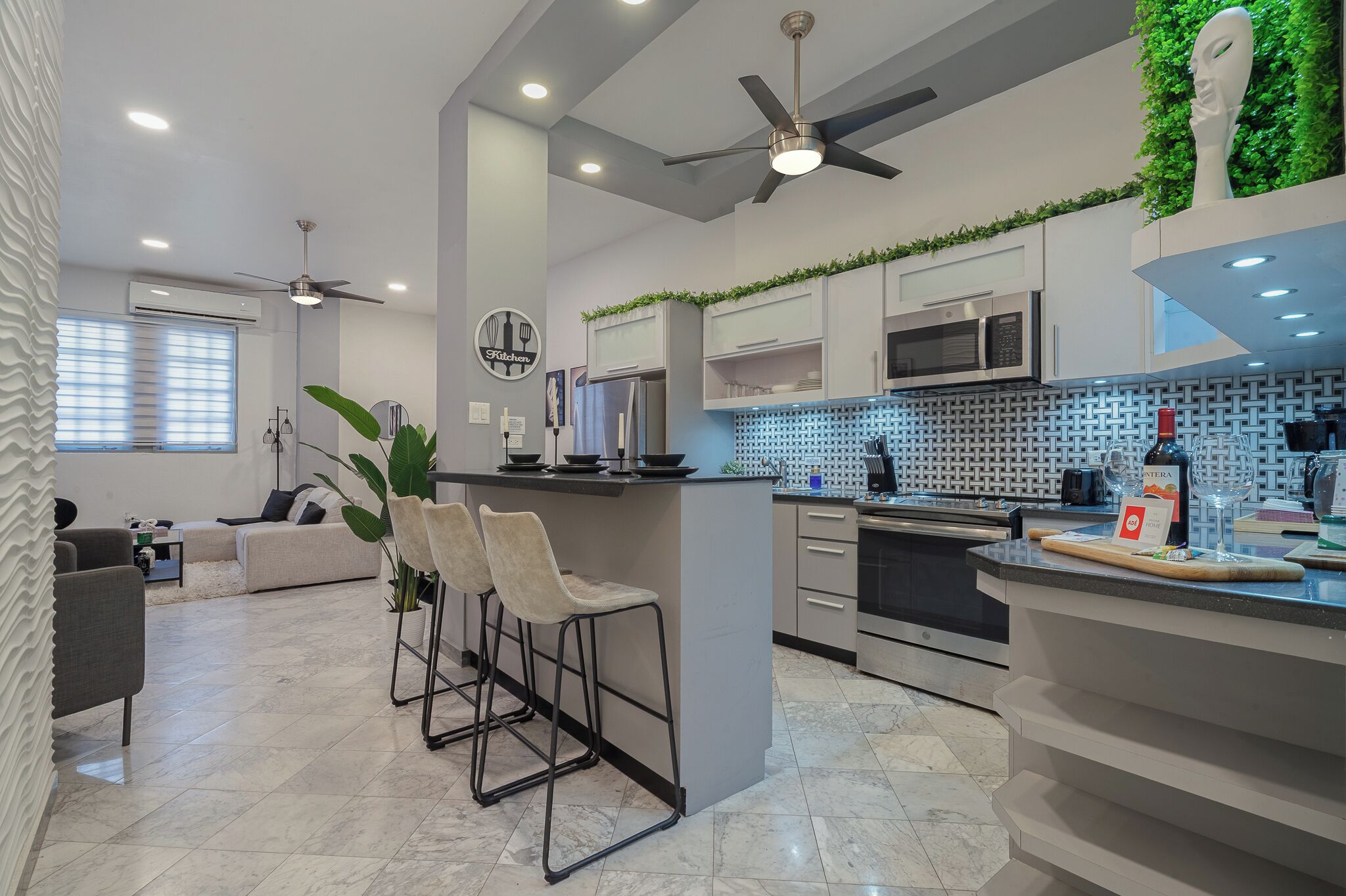 Una cocina moderna con una isla central, taburetes de bar y un área de comedor con sofá.