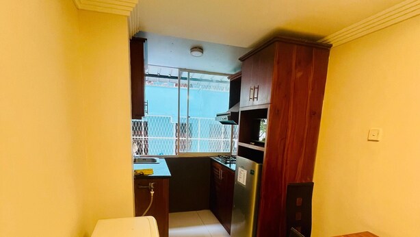 A compact kitchen with a refrigerator, stove, and wooden cabinets. - New York Guest House and Restaurant Colombo 06 (Colombo)