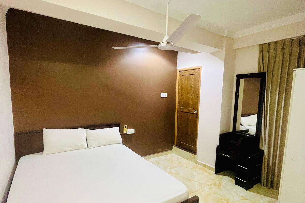 A hotel room with a large bed, a ceiling fan, a wardrobe, and a mirror.