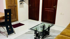 A living room with a glass coffee table, a sofa, a TV mounted on the wall, and two wooden doors. - New York Guest House and Restaurant Colombo 06 (Colombo)