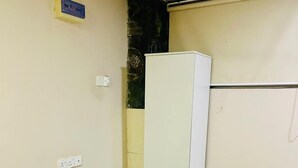 A small, clean room with a white refrigerator, a black desk, and a white table. There is a wall socket and a small sign on the wall. - New York Guest House and Restaurant Colombo 06 (Colombo)
