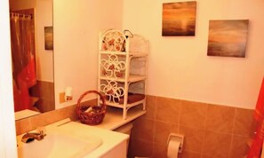 Un baño con lavamanos, inodoro y un estante blanco con toallas y una cesta.