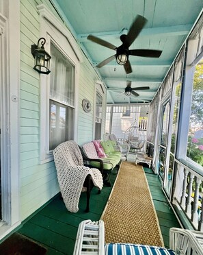 Eine überdachte Veranda mit Deckenventilator, Korbstühlen, einer Bank und einem Willkommensschild.