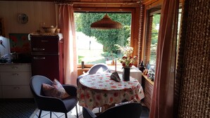 A cozy kitchen with a dining area, wooden ceiling, and a view of greenery outside.