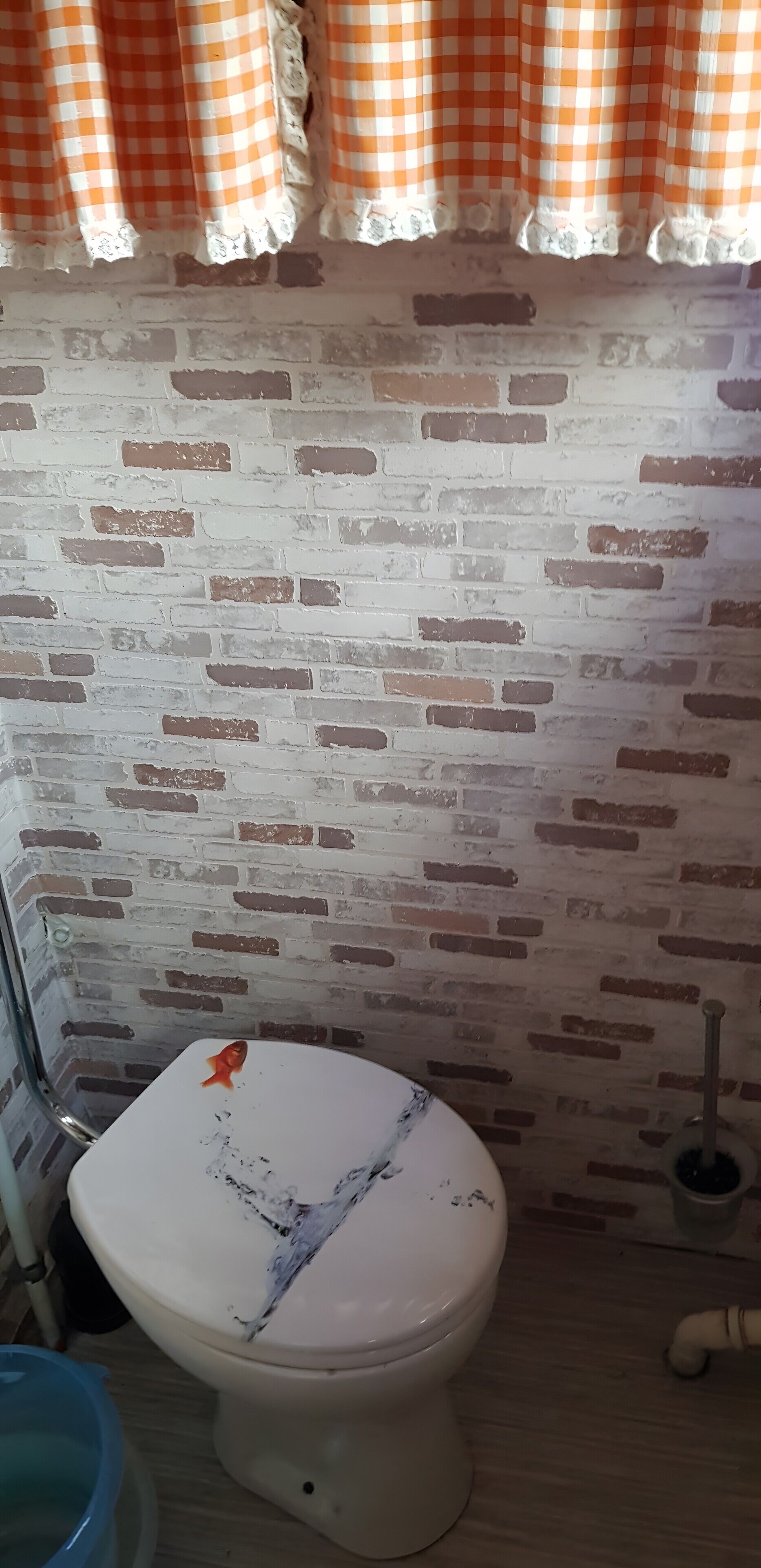 Un bany amb un vàter blanc, una paret amb relleu de rajola i una cortina de quadres.