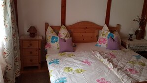 A bedroom with a wooden headboard, floral bedding, a bedside table with a lamp, and a nightstand with a vase of flowers.
