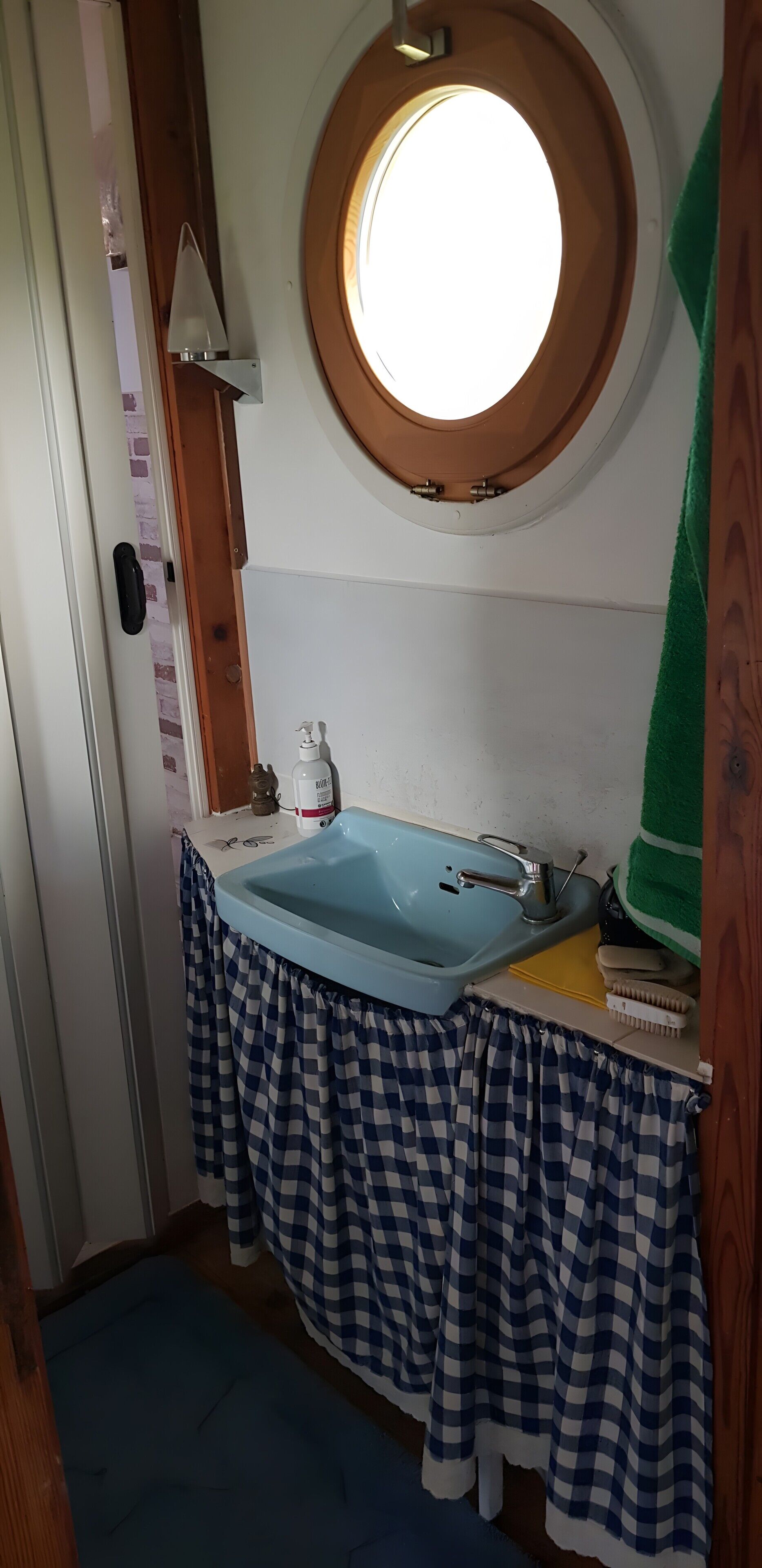 A bathroom with a round window, a sink, and a checkered cloth covering.