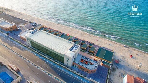 Vista aérea de un hotel costero que cuenta con un edificio grande, un estacionamiento y una playa con tumbonas.