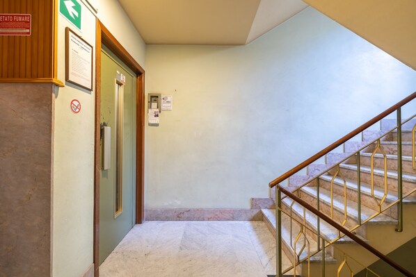 A hallway with a green door, a no-smoking sign, and a staircase with marble steps.