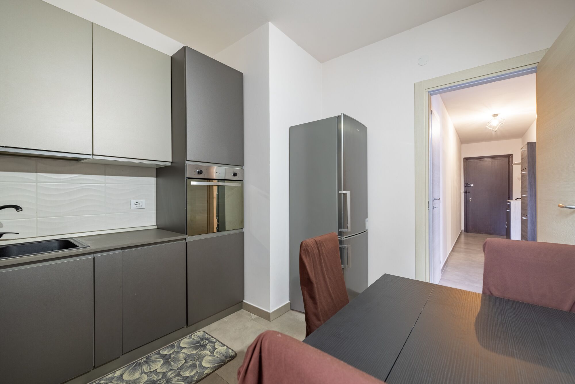 A modern kitchen with grey cabinets, a stainless steel range hood, and a built-in oven.