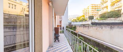 Un balcón con piso a cuadros, baranda de metal y vista de edificios vecinos.