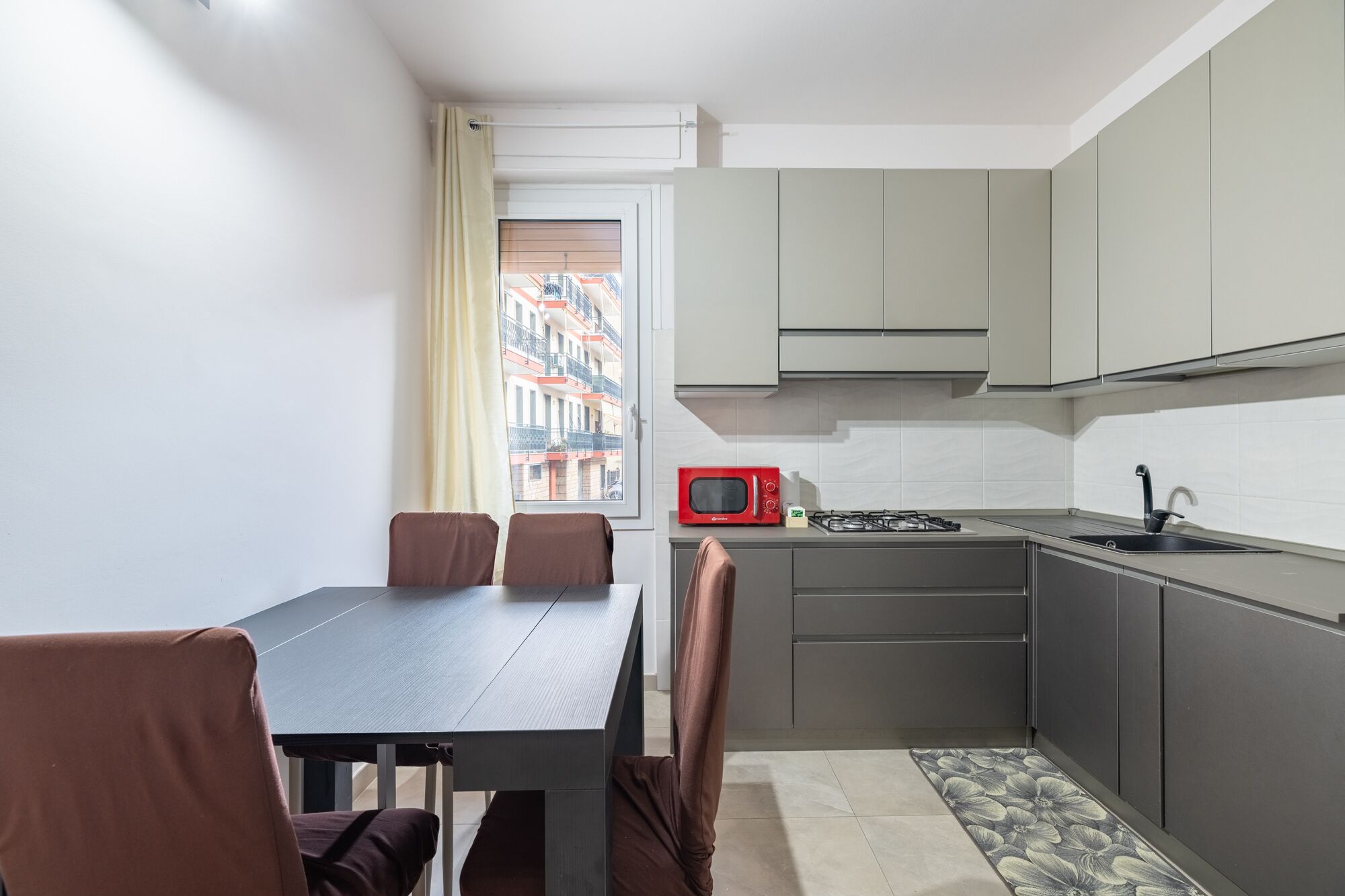 A compact kitchen with a dining table, chairs, a red microwave, and a gas stove.