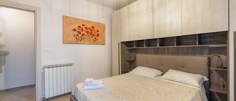 A bedroom with a bed, a radiator, a painting, and a wooden headboard.