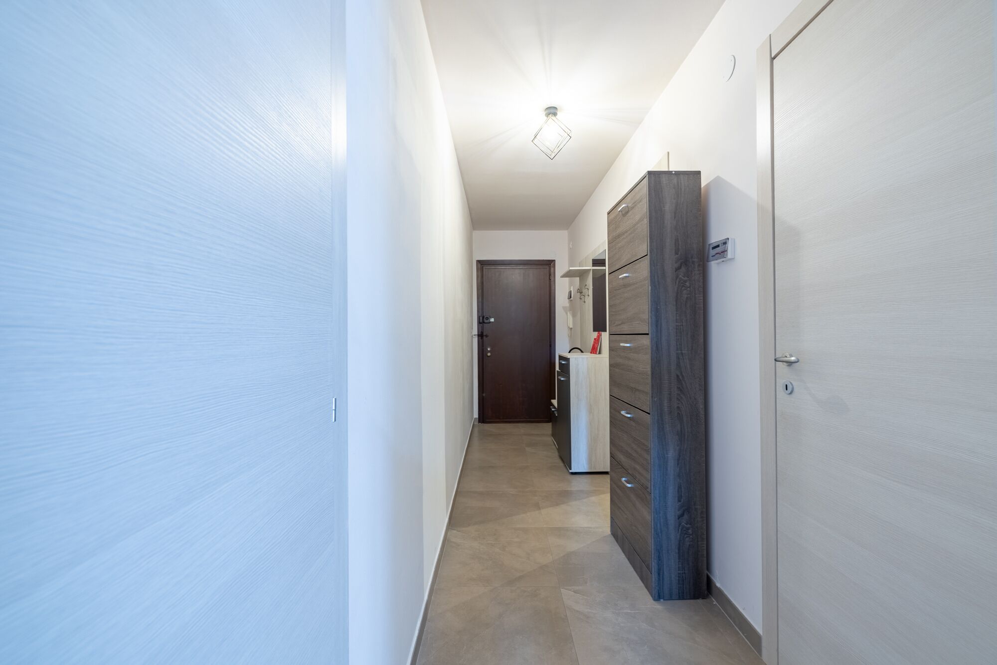 A narrow hallway with a door at the end, a wardrobe with multiple drawers, and a light fixture on the ceiling.