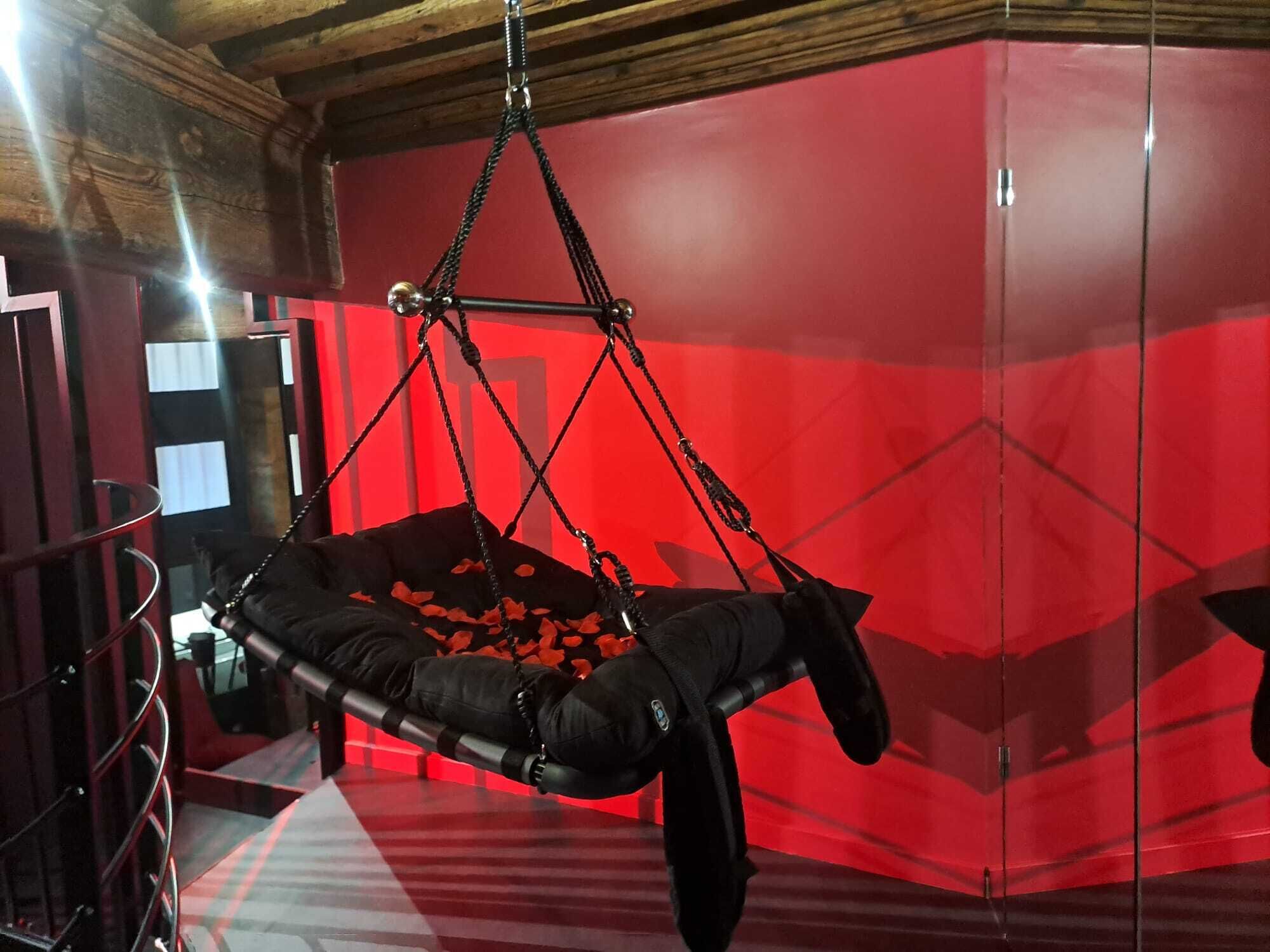Ein Zimmer mit Hängesessel, Rosenblättern, roter Wand und Holzboden.