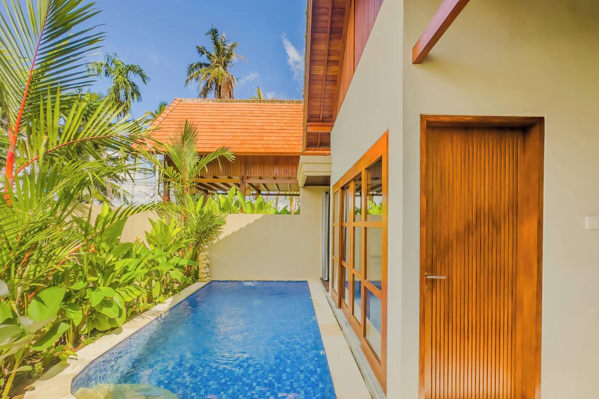 A swimming pool with a tiled edge, surrounded by lush greenery and a wooden door.