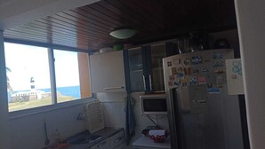 A compact kitchen with a window overlooking a lighthouse, a microwave, a refrigerator, and a sink.