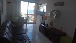A living room with a leather couch, a small table, and a chair. There is a balcony with a view of the ocean.