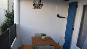 A small outdoor patio with a wooden table and two chairs, a potted plant, and a blue door. - L' Escale, appartement climatisé à 50 mètres de la plage avec WIFI et Box Tv (Fos-sur-Mer)