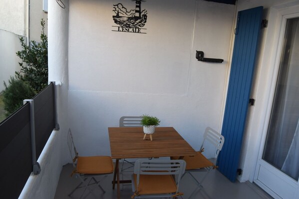 Eine kleine Terrasse im Freien mit einem Holztisch, zwei Stühlen, einem Blumentopf und einer blauen Tür.