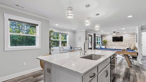 Une cuisine moderne dotée d’un grand îlot central, de luminaires suspendus et offrant une vue sur l’extérieur.