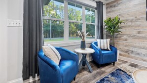 Un salon moderne avec deux fauteuils bleus, une petite table ronde et une grande fenêtre avec des rideaux.