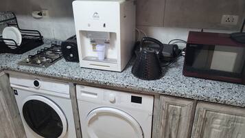 A kitchen with a washing machine, a coffee maker, a microwave, and a dish rack.