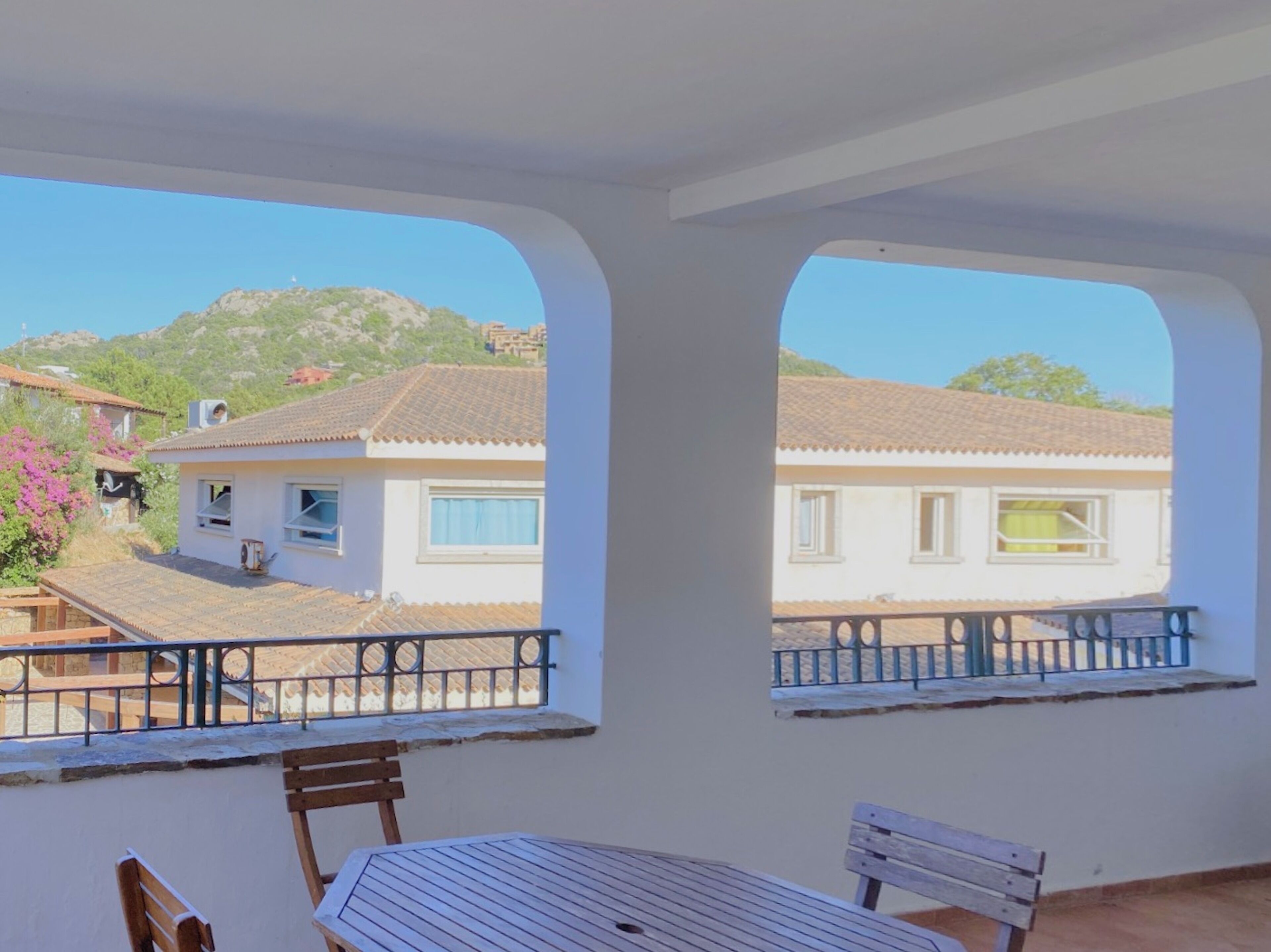 A room with a table and chairs, a window with a view of a house and a hill.