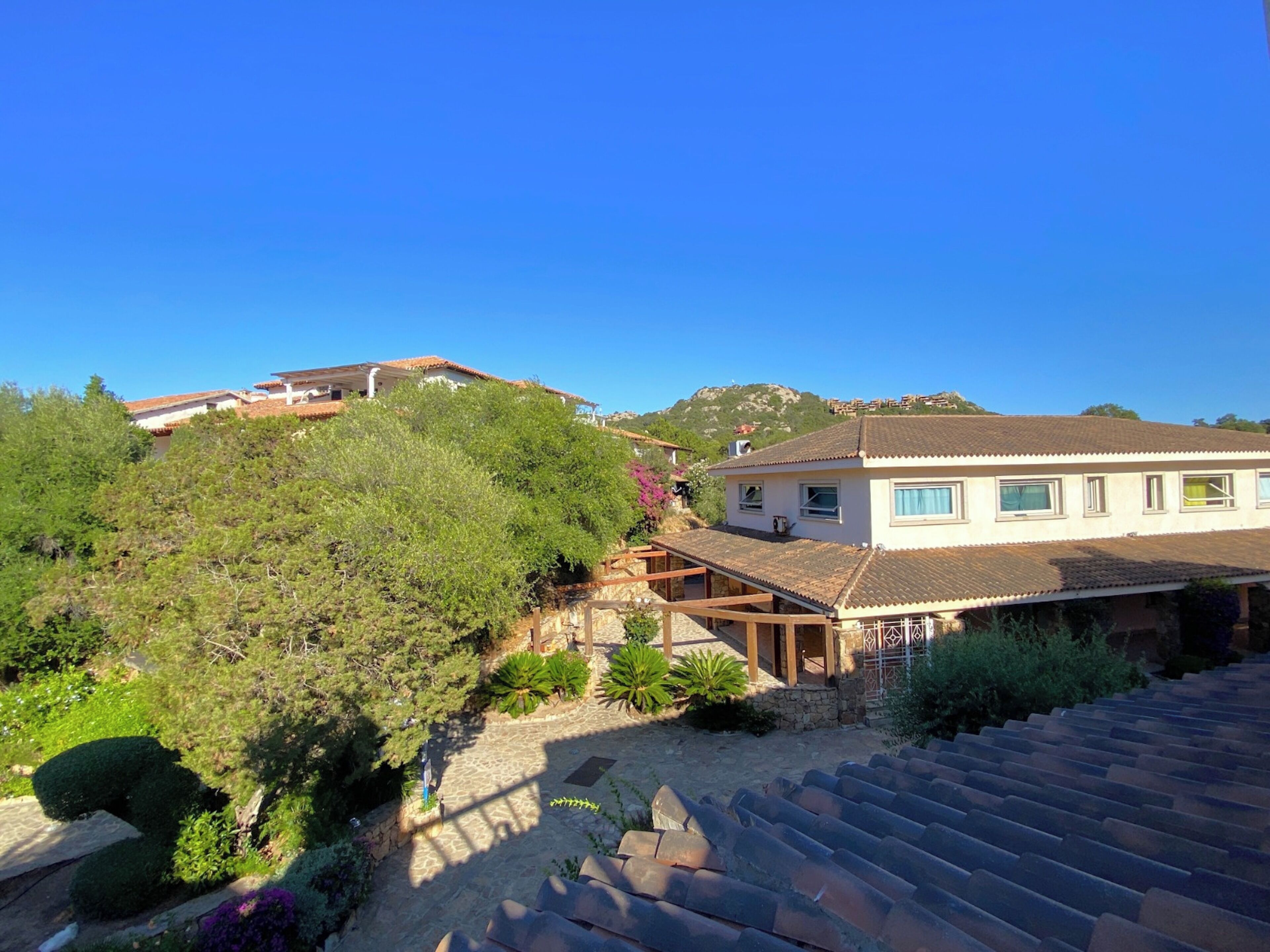 A hillside property with a house featuring a tiled roof, a stone pathway, and lush greenery.