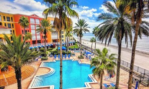 Um resort com uma piscina grande, palmeiras e vista para a praia.