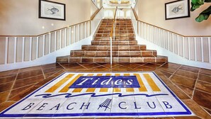 Una escalera conduce a un área de club de playa con piso de baldosas que muestra el nombre del club.