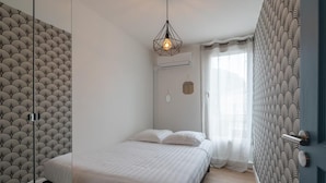 A bedroom with a bed, a hanging light fixture, and patterned wallpaper.