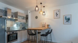 A modern kitchen with a wooden countertop, black bar stools, and pendant lighting.