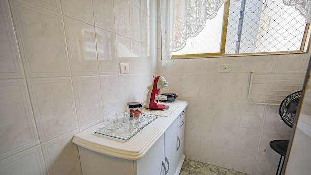 A small kitchen with white cabinets, a countertop, and a window with lace curtains.