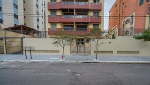 A multi-story building with a gated entrance, a small tree in front, and a bench to the left.