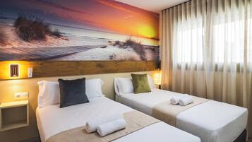 A hotel room with two beds, a sunset mural, and a window with curtains.