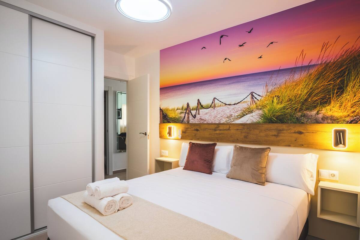 Une chambre d’hôtel avec un grand lit, un tableau représentant une scène de plage et une vue sur la mer.